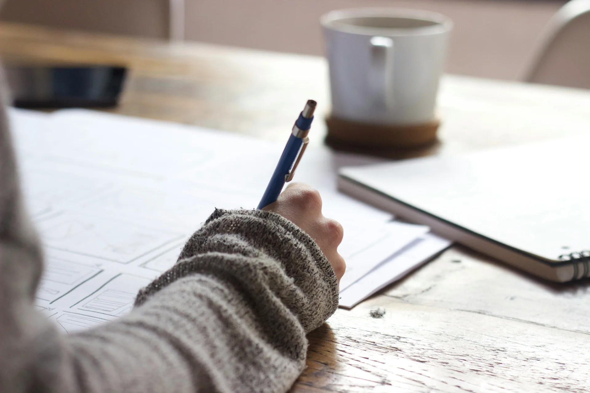 A person writing in a journal at a warm wooden desk