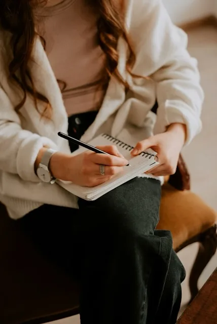 A person quietly writing in a journal while sitting in an armchair